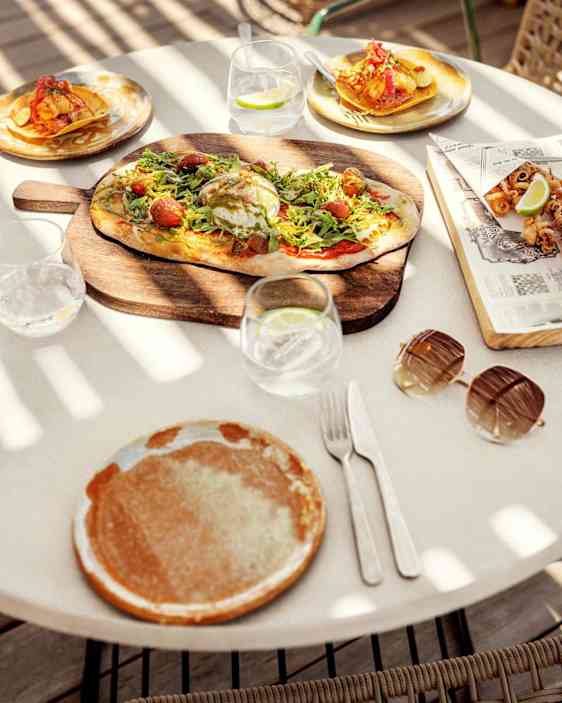 Ruoka katettuna pöydälle, jolla valmiina lautaset, lasit ja aterimet.