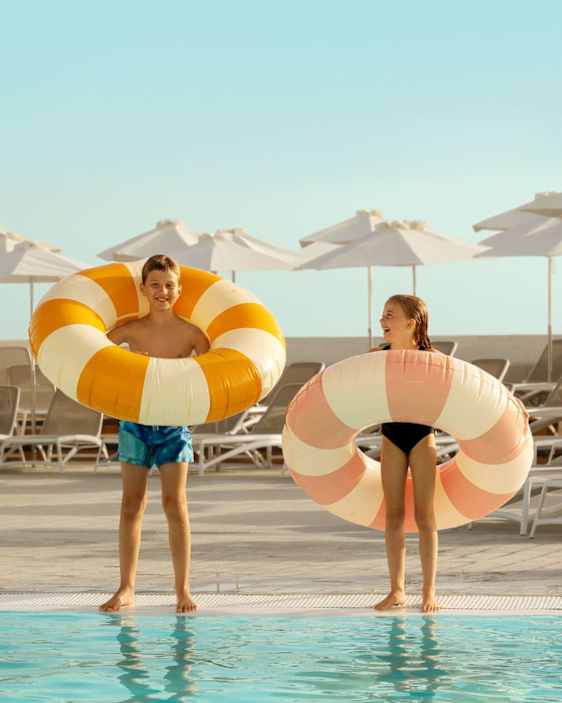 Kaksi lasta seisomassa altaan reunalla isot raidalliset uimarenkaat ympärillään