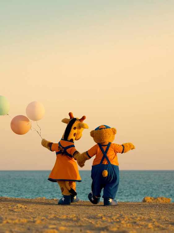 Lollo ja Bernie kävelevät käsi kädessä rannalla auringonlaskussa, Lololla on kädessään ilmapalloja.