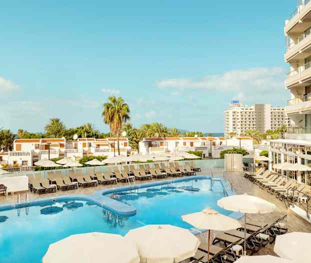 Näköala hotellin uima-altaaseen aurinkotuoleineen ja varjoineen, ympäröitynä rakennuksilla ja palmuilla. (Tekoälyn luoma teksti)