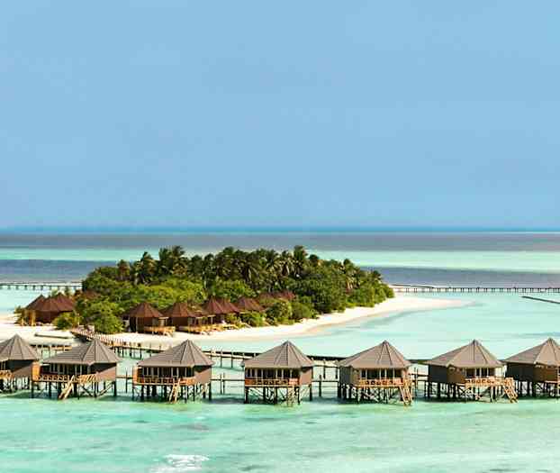 Useita palkeilla seisovia bungaloweja veden päällä vehreän saaren vieressä. (Tekoälyn luoma teksti)