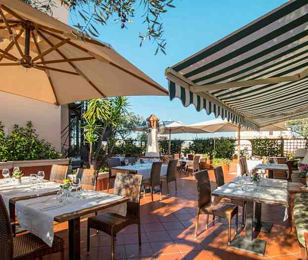 Ulkoterassi, jossa on pöytiä ja tuoleja aurinkovarjojen ja markiisin alla. (Tekoälyn luoma teksti)