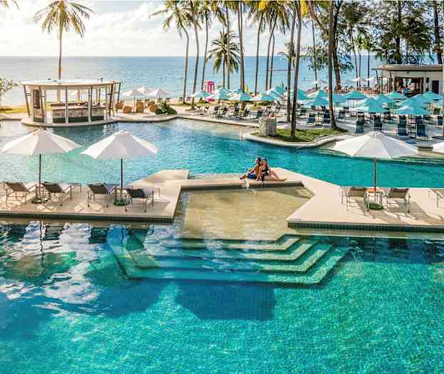 Suuri uima-allas aurinkotuoleineen ja aurinkovarjoineen, näkymä merelle, palmujen ympäröimänä. (Tekoälyn luoma teksti)