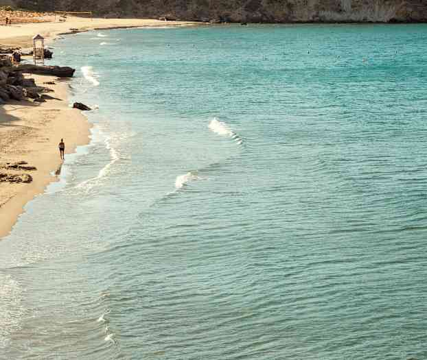 Ranta kirkasta vettä ja henkilö kävelee rantaviivan tuntumassa. (Tekoälyn luoma teksti)