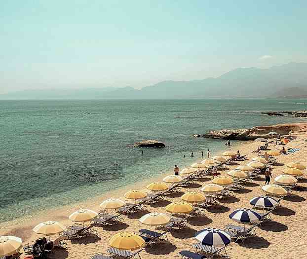 Ranta, jossa on aurinkovarjoja ja aurinkotuoleja meren rannalla. (Tekoälyn luoma teksti)