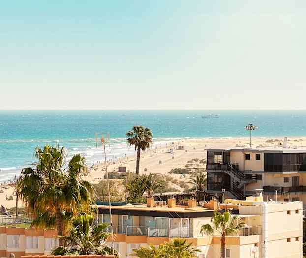 Näkymä hiekkarannalle, merelle, palmuihin ja rakennuksiin. (Tekoälyn luoma teksti)