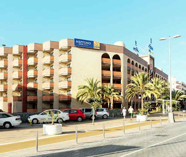 Monivärinen rakennus, jossa on kyltti "NEPTUNO HOTEL", ympäröitynä palmuilla ja pysäköidyillä autoilla. (Tekoälyn luoma teksti)