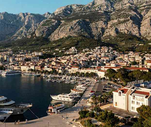 Näkymä satamasta veneineen ja kaupungista, jonka taustalla on vuoria. (Tekoälyn luoma teksti)