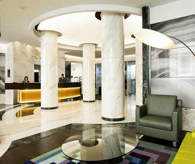 Moderni hotellin aula, jossa marmorisarakkeita, vastaanottotiski ja istuinryhmä. (Tekoälyn luoma teksti)