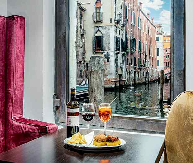 Pöytä, jossa juomia ja välipaloja, taustalla näkyy kanava ja rakennuksia. (Tekoälyn luoma teksti)