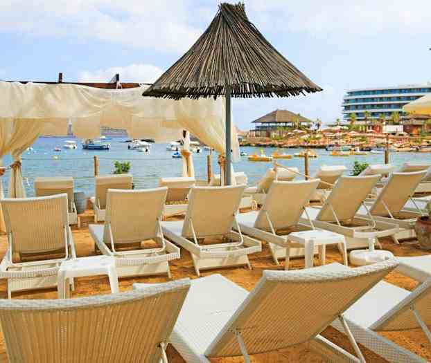 Ranta, jolla on aurinkotuoleja rauhallisen merenlahden edessä, jossa on veneitä. (Tekoälyn luoma teksti)