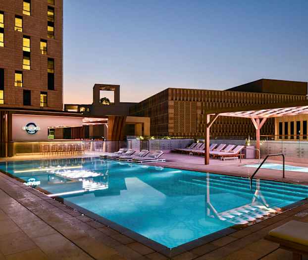 Valaistu ulkouima-allas illalla, ympärillä aurinkotuoleja ja modernia arkkitehtuuria. (Tekoälyn luoma teksti)