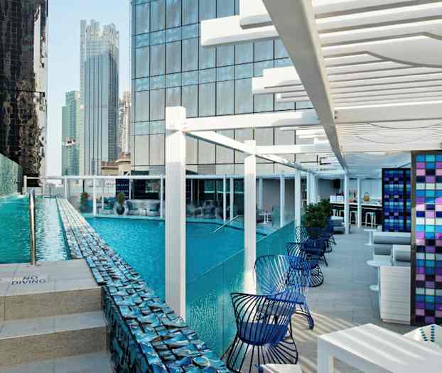 Nykyaikainen ulkouima-allas, jota ympäröivät korkeat rakennukset, ja vieressä istuma-alue. (Tekoälyn luoma teksti)