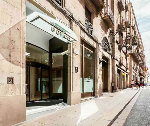 Rakennuksen sisäänkäynti lasiovilla, sijaitsee kadulla, jota reunustavat rakennukset molemmin puolin. (Tekoälyn luoma teksti)