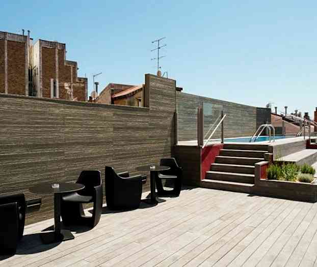 Kattoterassi, jossa puurakenteinen lattia. Mustia tuoleja ja pöytiä edessä. Portaat johtavat uima-altaalle. (Tekoälyn luoma teksti)