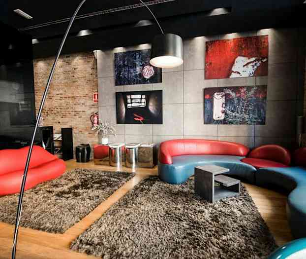 Moderni huone, jossa on erikoismuotoinen sinipunainen sohva, punainen huuliensuuruinen istuin sekä seinällä taideteoksia. Lattialla on beigeltapeet. (Tekoälyn luoma teksti)