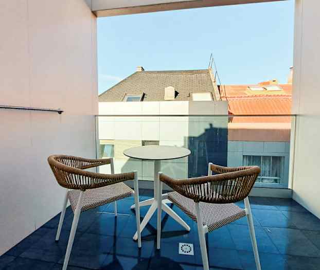 Kaksi tuolia ja pöytä parvekkeella, näkymä kattoihin. (Tekoälyn luoma teksti)