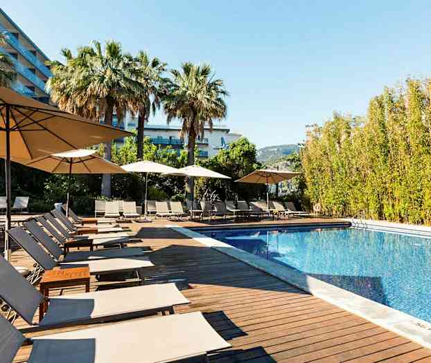 Ulkouima-allas, jonka ympärillä aurinkotuoleja ja aurinkovarjoja, ympärillä palmuja ja puita. (Tekoälyn luoma teksti)