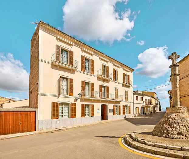 Katu, jossa on vaalea julkisivurakennus ja kivipylväs, jossa on risti. (Tekoälyn luoma teksti)