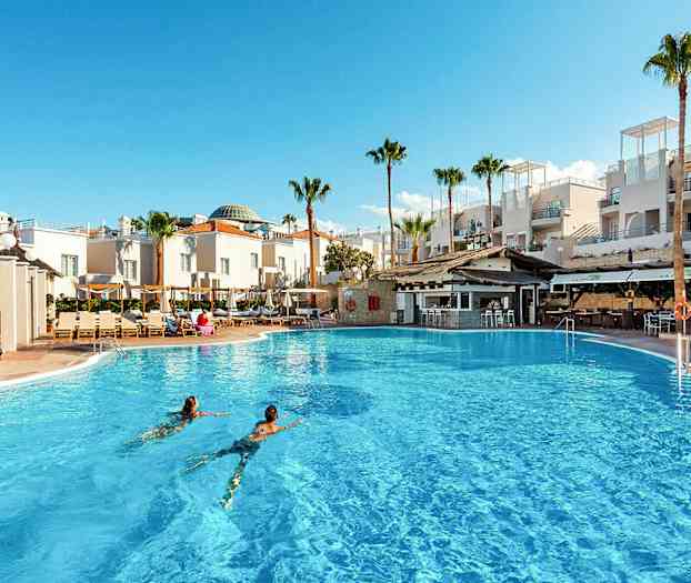 Suuri ulkouima-allas valkoisten rakennusten ja palmujen edessä. (Tekoälyn luoma teksti)