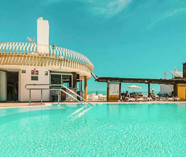 Ulkouima-allas rakennuksen lähellä, jossa on aurinkotuoleja ja kirkas sininen taivas. (Tekoälyn luoma teksti)