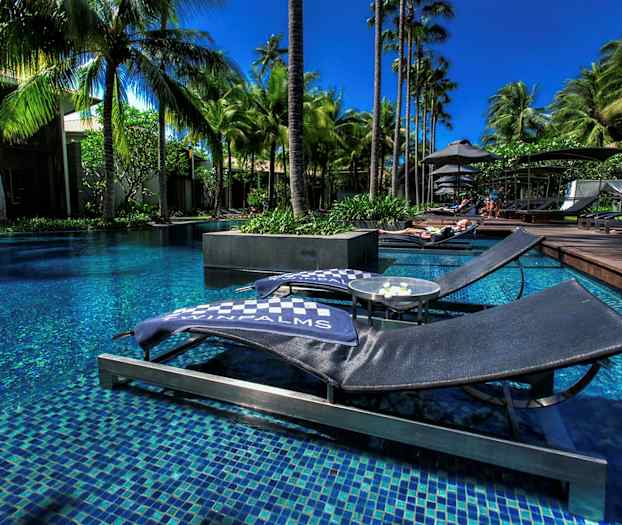 Kuva rantatuoleista uima-altaan äärellä, ympärillä palmuja. (Tekoälyn luoma teksti)