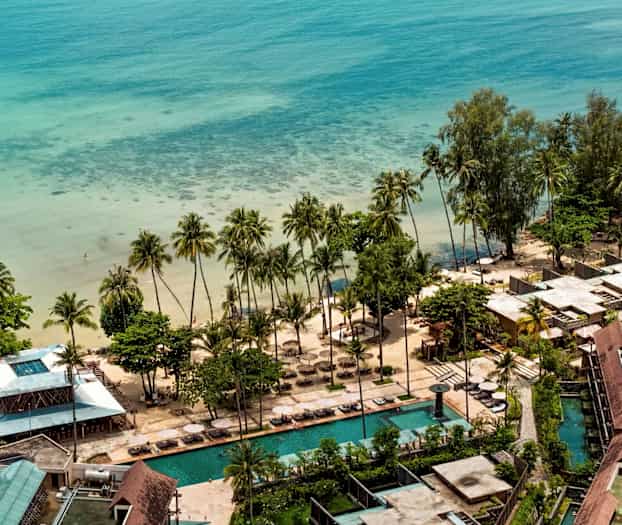 Ilmakuva rantakohteesta meren rannalla, jossa on palmuja, hiekkaranta ja uima-altaita. (Tekoälyn luoma teksti)