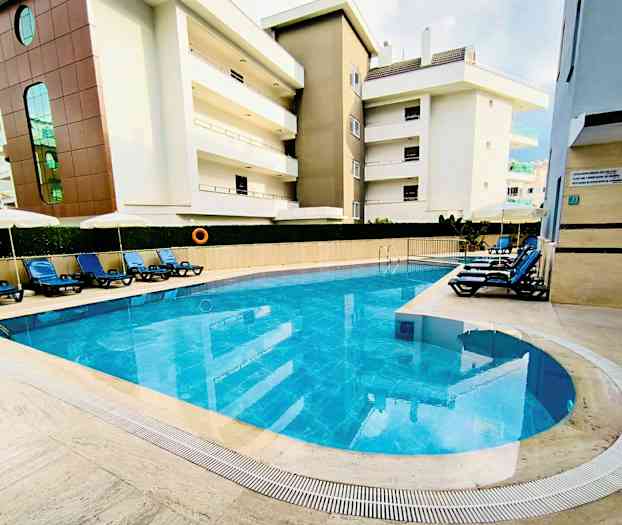 Ulkouima-allas sinisellä vedellä, jota ympäröivät aurinkotuolit ja rakennukset. (Tekoälyn luoma teksti)