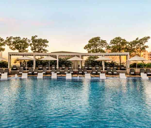 Ulkouima-allas, jota ympäröivät aurinkotuolit ja aurinkovarjot, taustalla puita. (Tekoälyn luoma teksti)