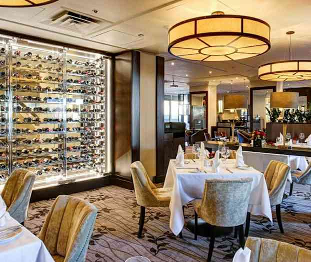 Ravintola, jossa on katettuja pöytiä ja seinä täynnä viinipulloja. (Tekoälyn luoma teksti)