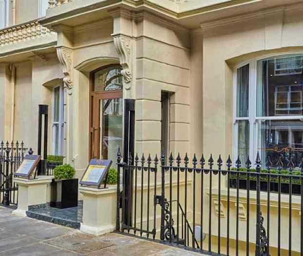 Rakennuksen sisäänkäynti, jossa koristeellinen julkisivu ja metalliaita. (Tekoälyn luoma teksti)