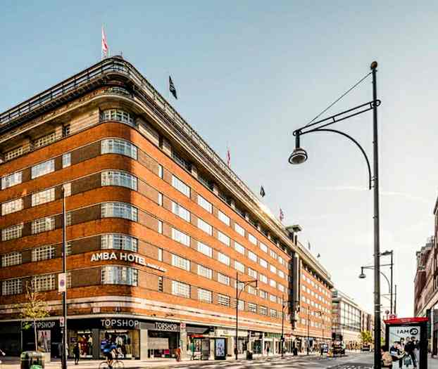 Suuri tiilirakennus, jonka yläosassa liput ja katutasolla kauppoja. (Tekoälyn luoma teksti)