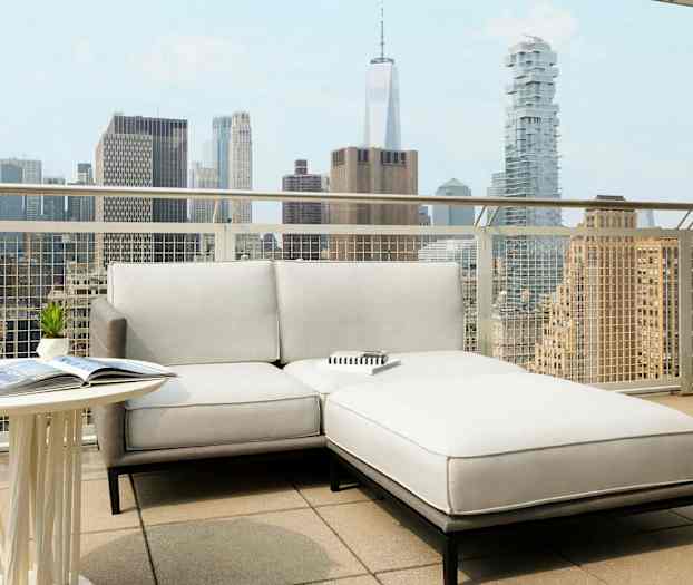 Terassi, jossa on vaalea sohva ja pöytä, kaupunkimaiseman taustalla. (Tekoälyn luoma teksti)