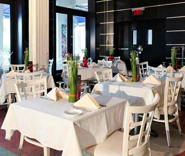 Tyylikäs ravintola-alue, jossa on valkoisia pöytiä ja tuoleja sekä kukkakoristeluja. (Tekoälyn luoma teksti)