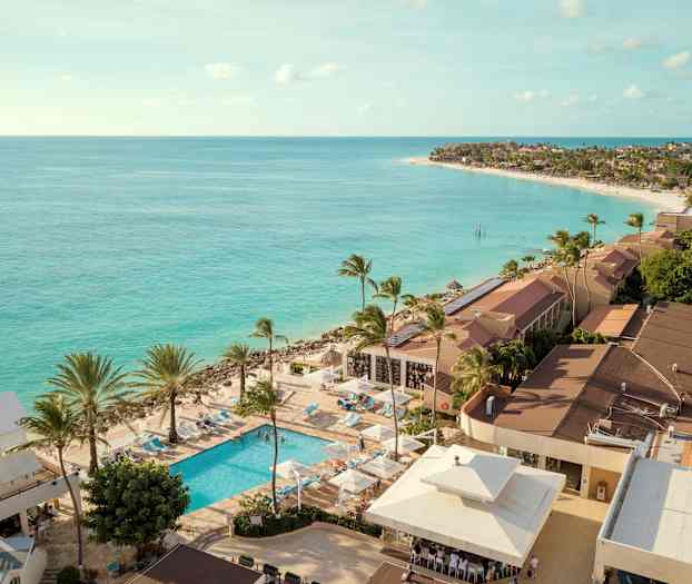 Näkymä ranta-alueesta, turkoosia merta, lomakeskus, jossa uima-allas ja palmuja. (Tekoälyn luoma teksti)