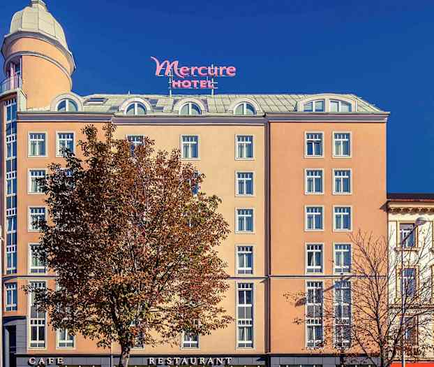 Hotellin Mercure ulkopuoli, jossa beige julkisivu, lukuisia ikkunoita ja korkea torni ylhäällä. (Tekoälyn luoma teksti)