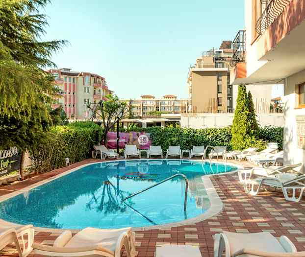 Ulkouima-allas, jota ympäröivät aurinkotuolit ja vehreys. Taustalla rakennuksia. (Tekoälyn luoma teksti)