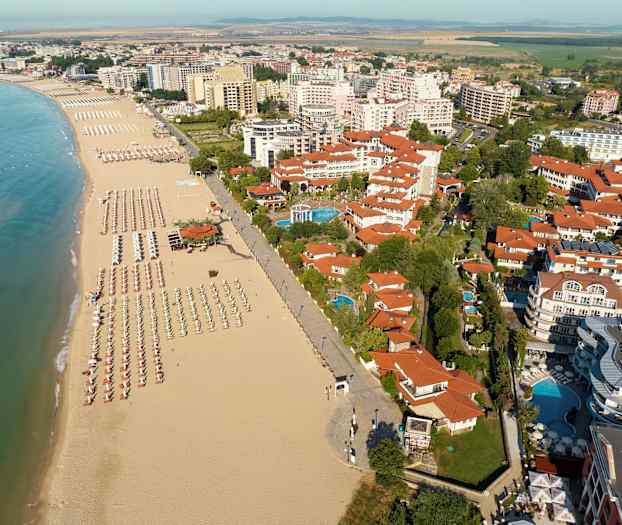 Näkymä rannalle, jossa on aurinkovarjoja ja aurinkotuoleja sekä ympäröivät rakennukset. (Tekoälyn luoma teksti)