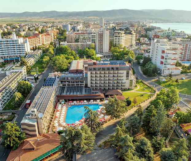 Ilmakuva hotellista uima-altaalla ja ympäröivistä rakennuksista vehreällä alueella. (Tekoälyn luoma teksti)