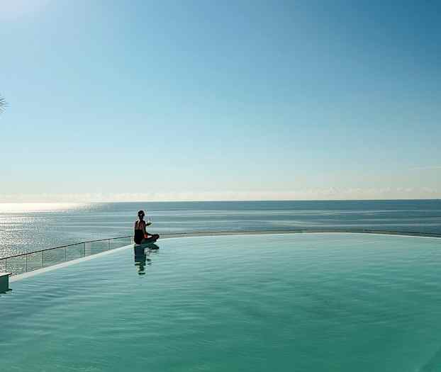 Henkilö istuu uima-altaan reunalla, taustalla näkyy meri. (Tekoälyn luoma teksti)