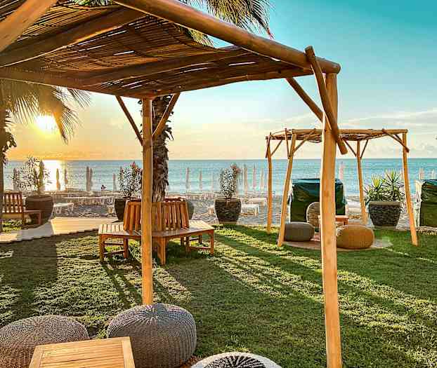 Puutarhakalusteet puurakennelmien alla lähellä rantaa auringonlaskun aikaan. (Tekoälyn luoma teksti)