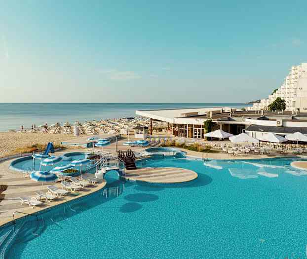 Kuva, jossa uima-allas, aurinkotuoleja ja aurinkovarjoja hotellin lähellä hiekkarantaa. (Tekoälyn luoma teksti)