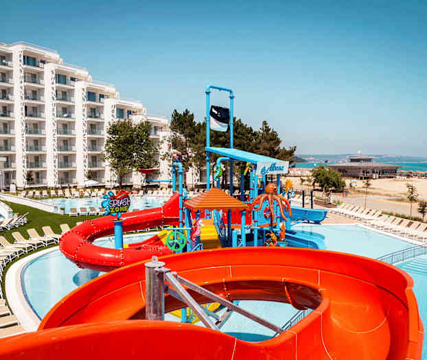 Kuva hotellialueesta, jossa on uima-allas, vesiliukumäkiä ja aurinkotuoleja lähellä rantaa. (Tekoälyn luoma teksti)