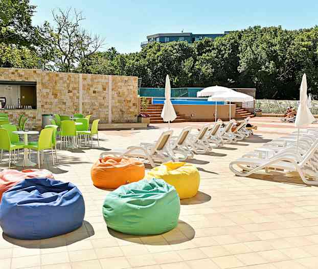 Aurinkotuoleja ja aurinkovarjoja uima-altaan äärellä, värikkäitä istuinpouffeja ja vihreitä tuoleja. (Tekoälyn luoma teksti)