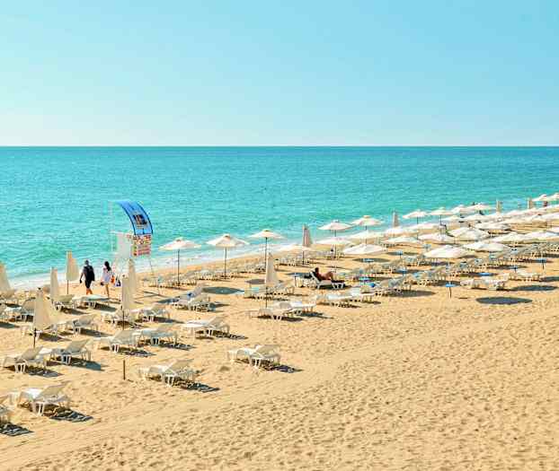 Ranta, jossa on aurinkotuoleja ja päivänvarjoja lähellä merta. (Tekoälyn luoma teksti)