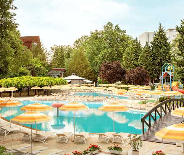 Uima-allasalue aurinkotuoleilla ja keltaisilla aurinkovarjoilla, vehreyden ympäröimänä. (Tekoälyn luoma teksti)