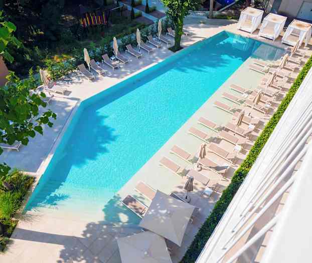 Kuva uima-altaasta, jota ympäröivät aurinkotuolit ja aurinkovarjot ulkoilmassa. (Tekoälyn luoma teksti)