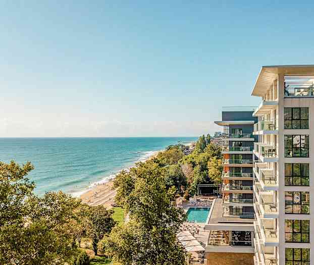 Näkymä korkealta rannikolle, oikealla hotelli ja ranta puiden ympäröimänä. (Tekoälyn luoma teksti)