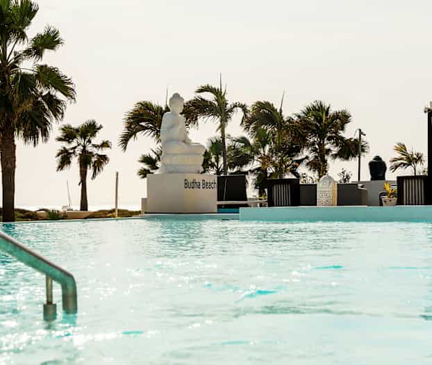 Ulkouima-allas, jossa istuva patsas ja ympärillä pergoloita sekä palmuja. (Tekoälyn luoma teksti)