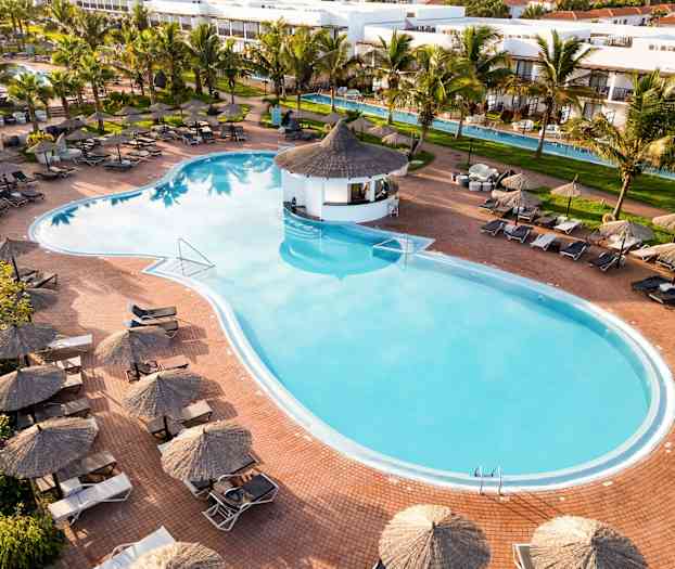 Näkymä suureen ulkouima-altaaseen, jota ympäröivät aurinkotuolit ja -varjot sekä vehreä puutarha. (Tekoälyn luoma teksti)